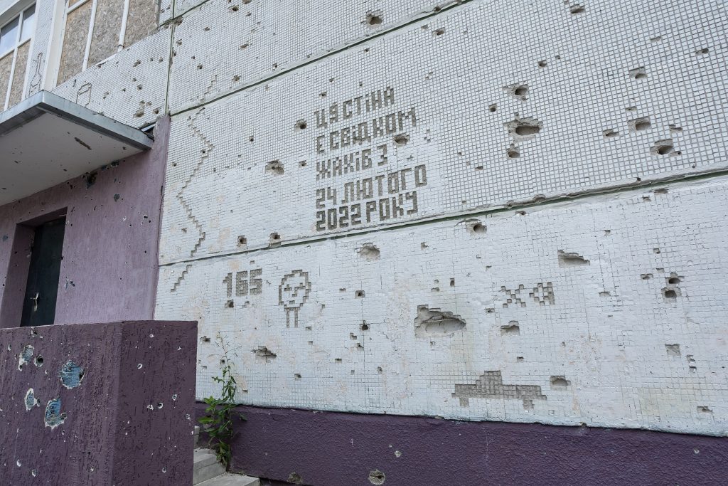 Фото роботи Віталія кохана на фасаді школи. Напис "Ця стіна є свідком жахів з 24 лютого 2022 року"