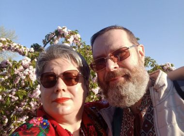 Галина та Олексій Ліпатови вишиванках і традиційних прикрасах фотографуються на фоні квітучої сакури.