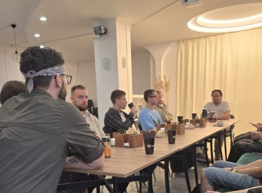 Група людей сидить за довгим дерев'яним столом у світлому приміщенні кафе на «Каві зі священником» від «Православних східняків»