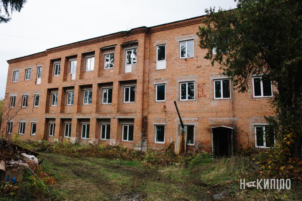 У Змієві реконструюють будинок під житло для ВПО: деталі проєкту Триповерхова цегляна будівля колишньої школи-інтернату у Змієві. На фасаді видно нові вікна, біля стін ростуть дерева та чагарники. Житло.