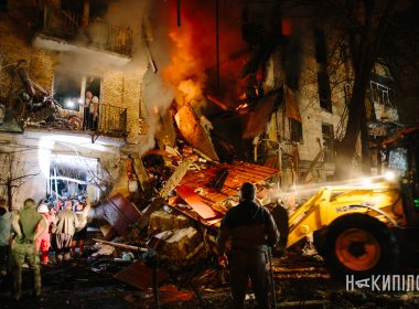 Люди стоять біля палаючих завалів під’їзду п’ятиповерхівки після російської атаки 12 жовтня в Холодногірському районі Харкова. Поруч — навантажувач. Фото: Павло Пахоменко для медіа «Накипіло».