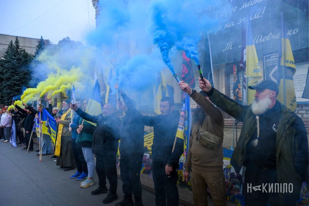 Прапори, спогади та дорога пам'яті: фоторепортаж з автопробігу в Харкові Люди під час хвилини мовчання стоять на тлі будівлі ХОДА з фаєрами