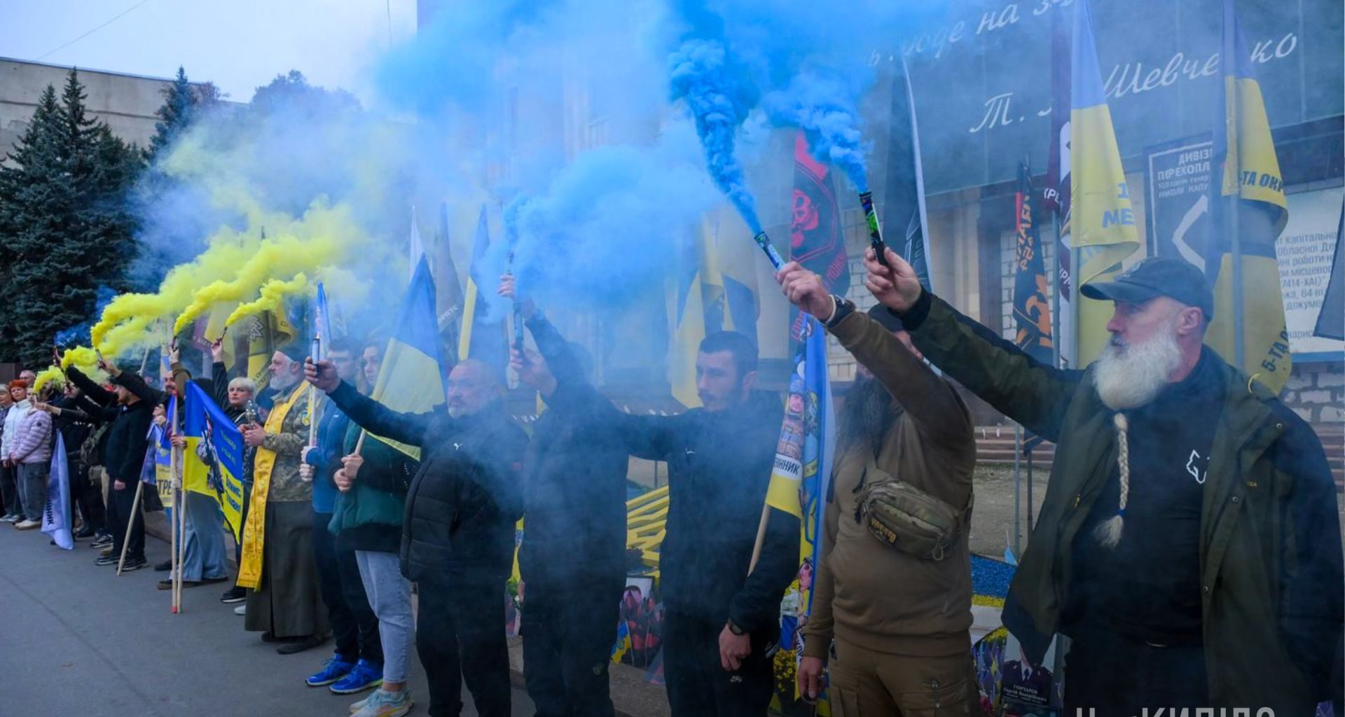 Люди під час хвилини мовчання стоять на тлі будівлі ХОДА з фаєрами